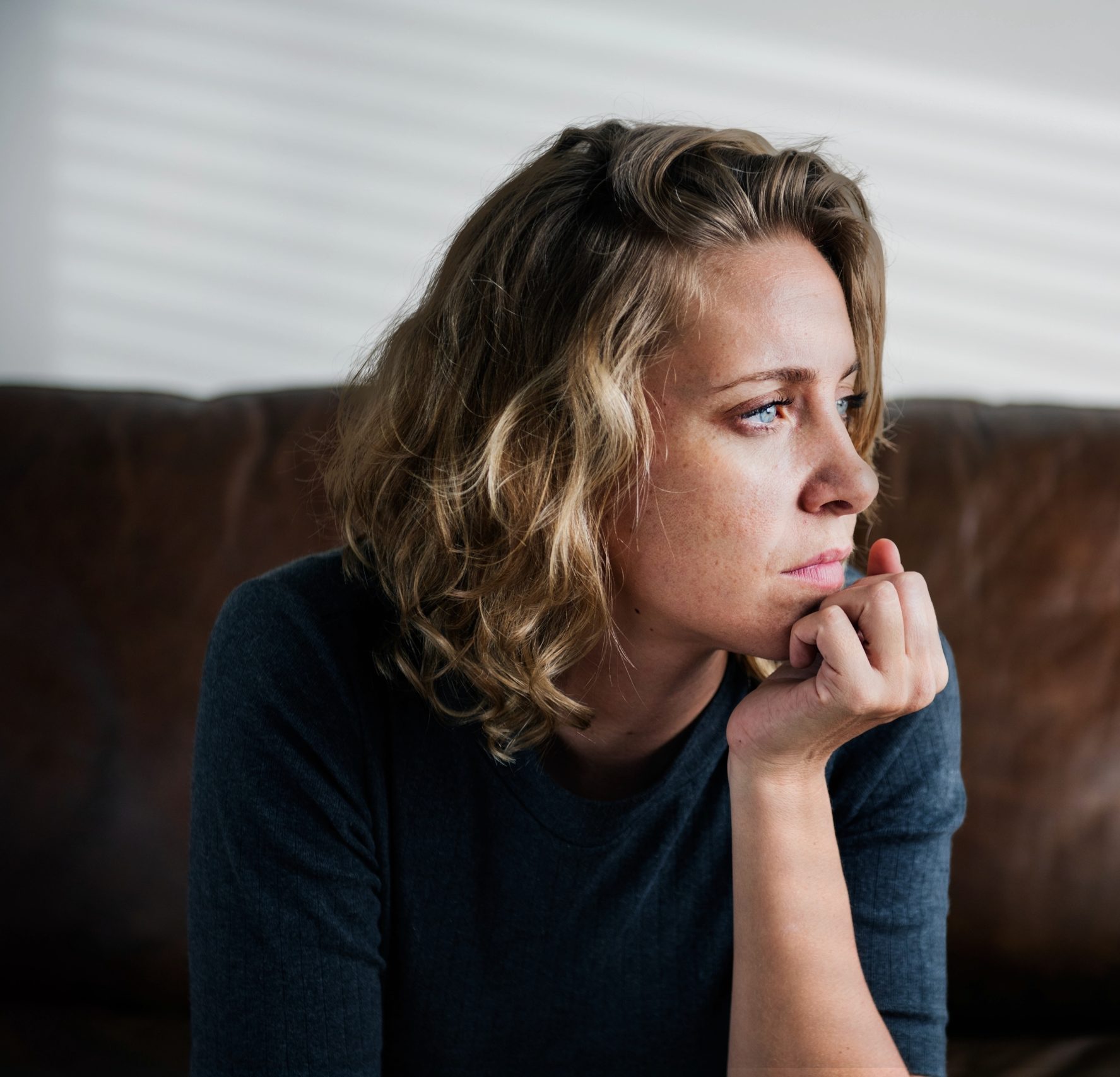 Woman with wavy blonde hair looking down pensively with hand near mouth
