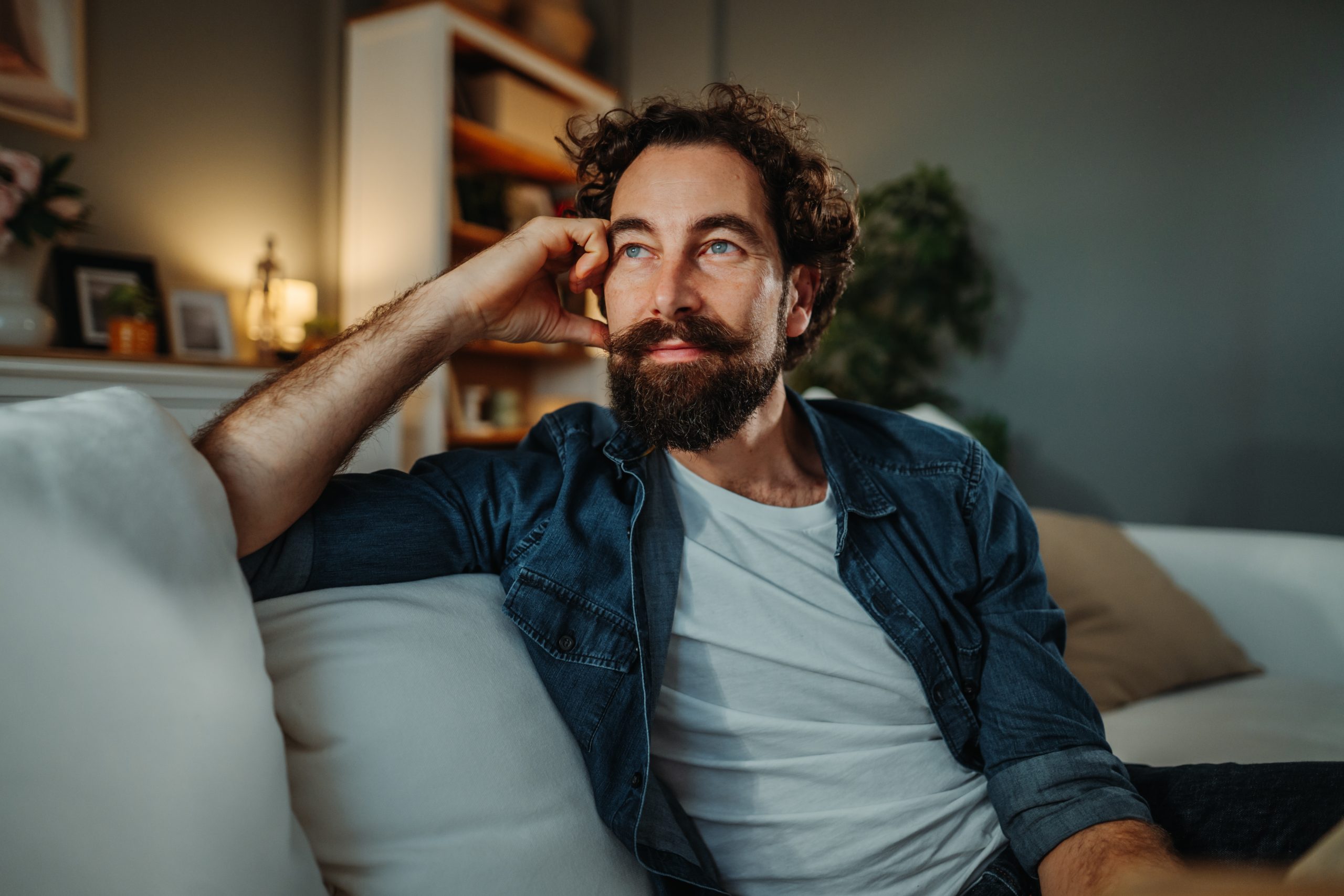 Man with beard resting head on hand while sitting on couch