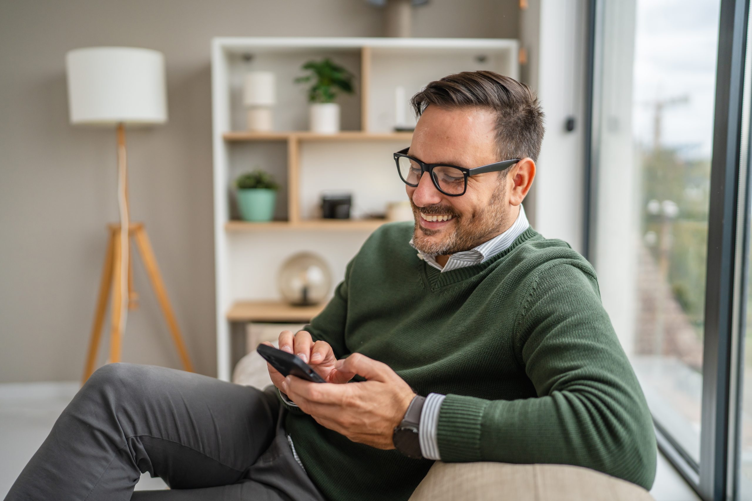 Man wearing glasses holding smartphone while sitting on couch at home