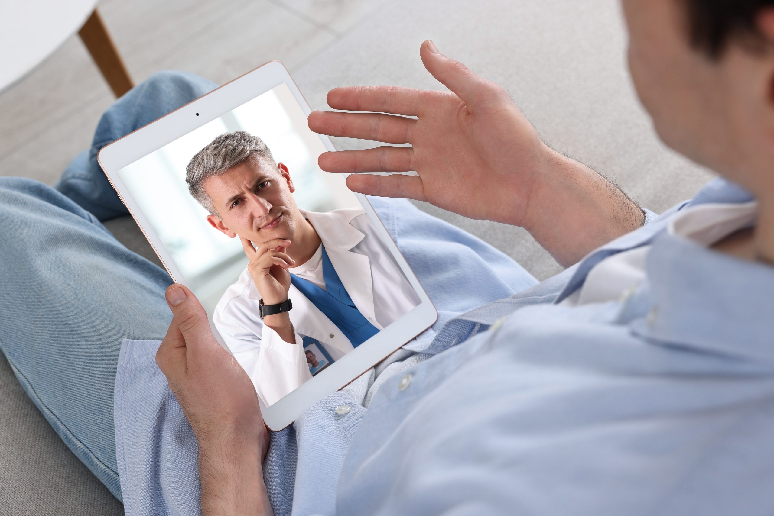 Patient holding tablet displaying doctor in white coat during telehealth video consultation
