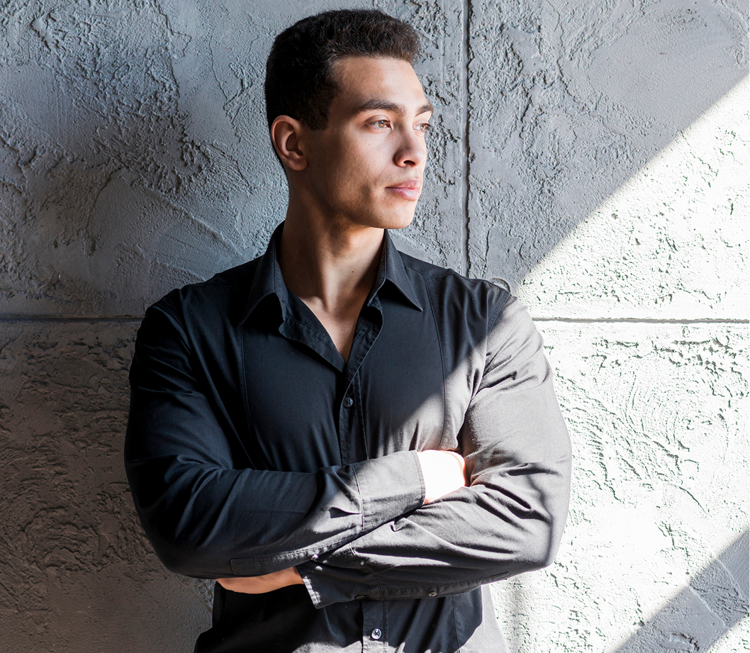 Man in dark shirt with arms crossed standing against textured concrete wall