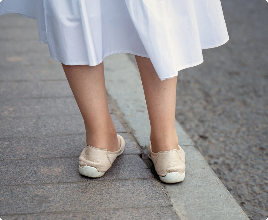 Person's feet showing inward-turning stance while wearing white dress and cream-colored shoes