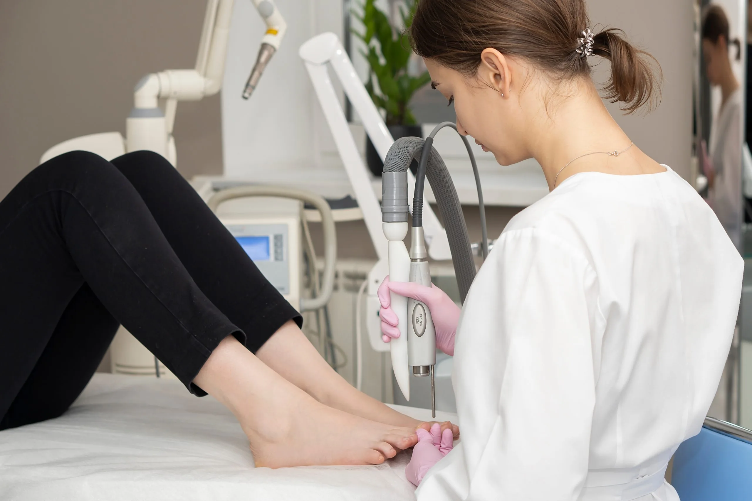 Podiatrist using pink handheld laser device on patient's foot during treatment