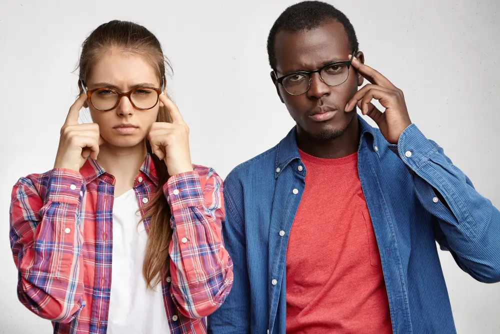 Teen girl and adult man both wearing glasses with hands to their heads, expressing concentration
