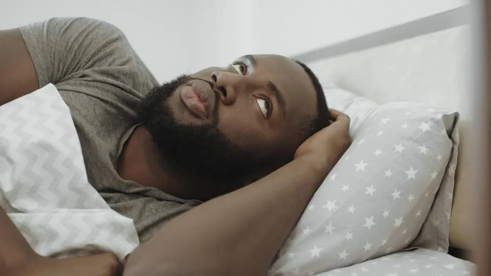 Man lying in bed looking frustrated and reluctant to wake up in the morning