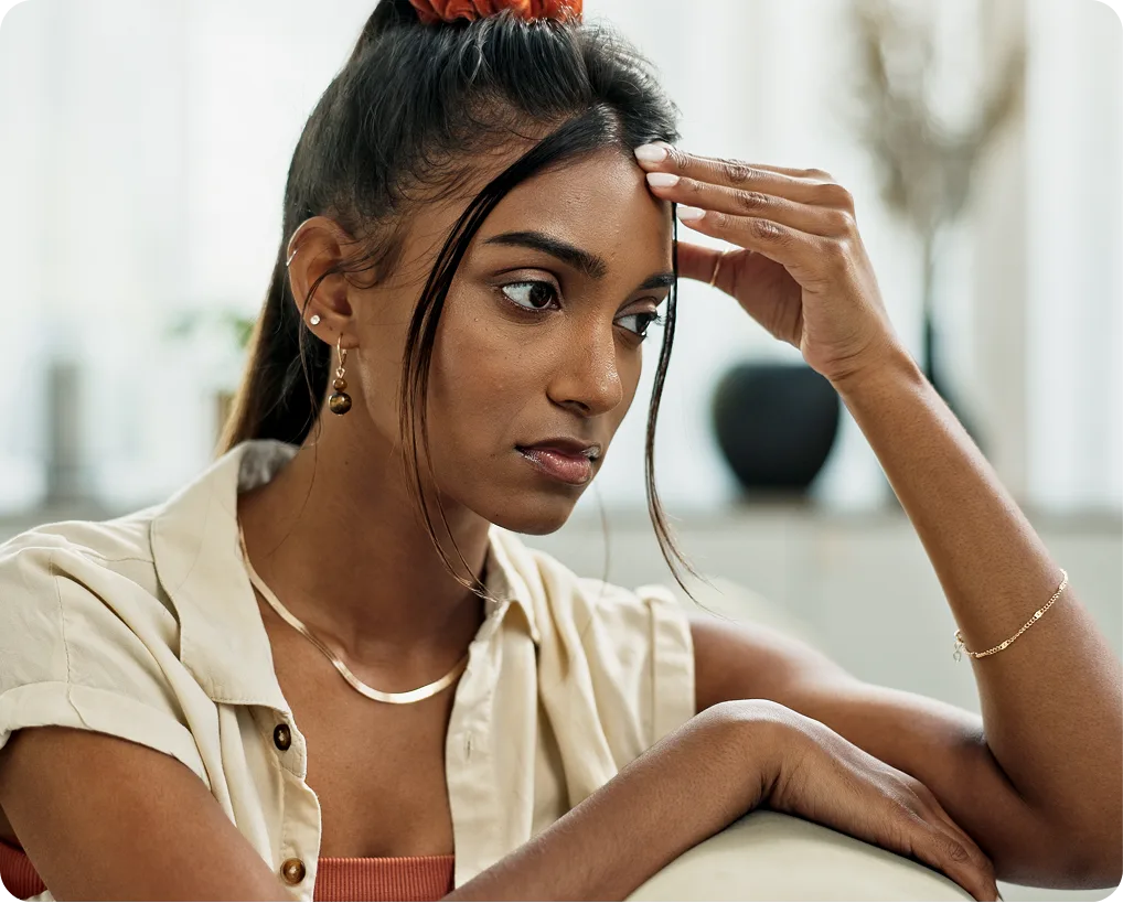 Woman with hand to forehead looking down, expressing worry or stress