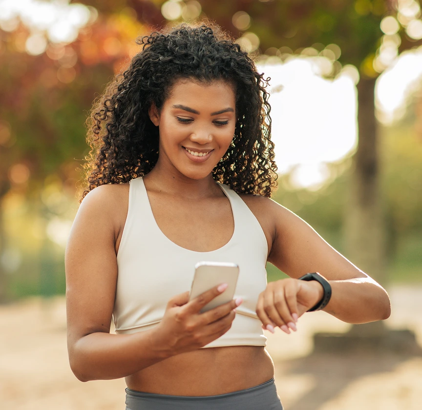 Woman in athletic wear checking her smartwatch while holding a phone outdoors