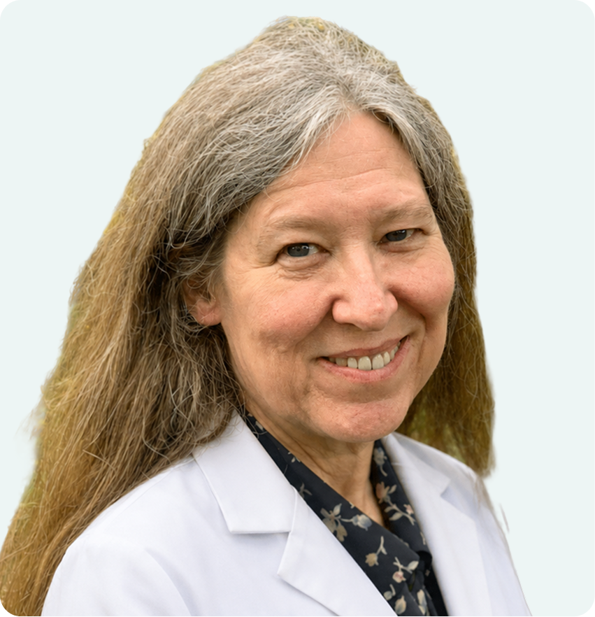 Healthcare provider with long gray hair wearing white coat over patterned scarf, smiling at camera