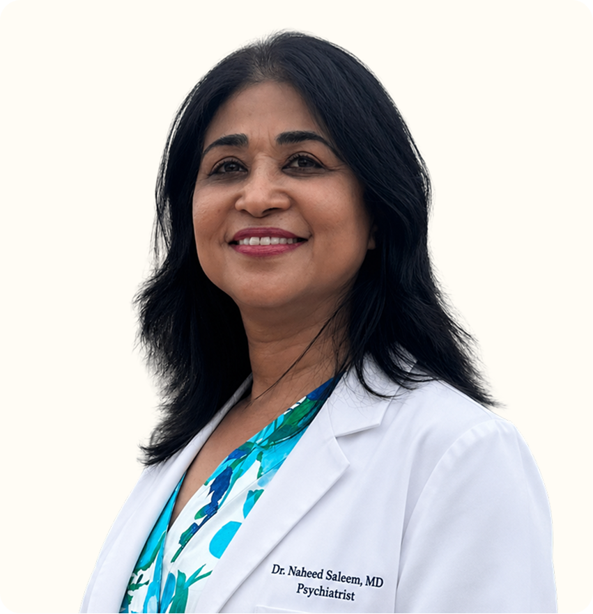 Dr. Naheed Saleem, MD Psychiatrist, wearing white coat over blue patterned top, smiling at camera