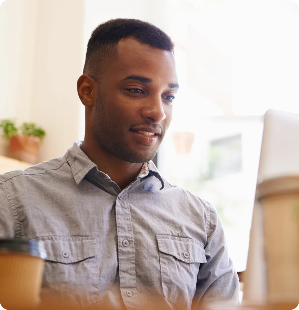 Man in gray shirt smiling while working at computer in bright office