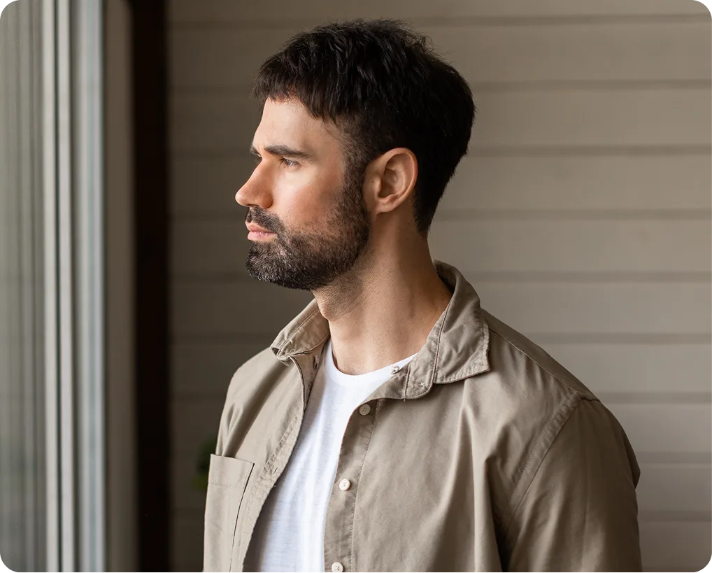 Man with dark beard in profile wearing beige jacket over white shirt