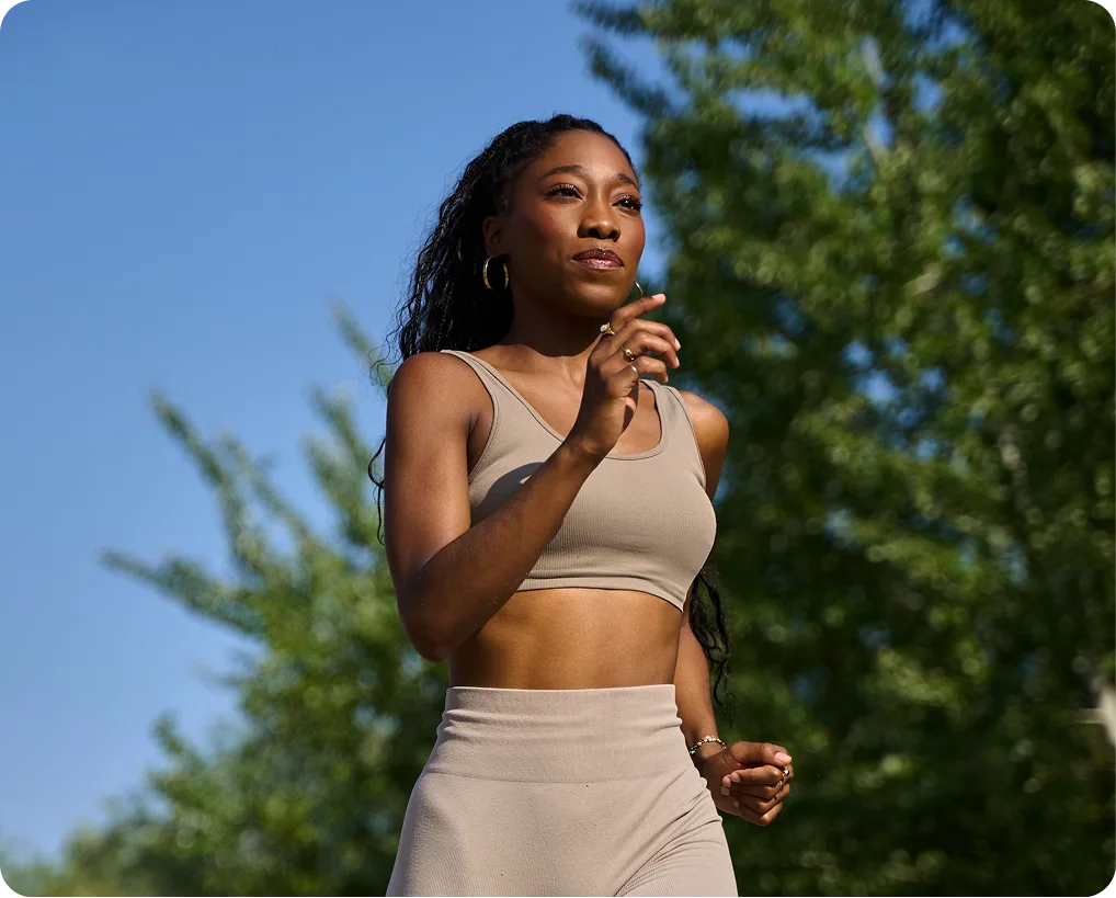 Woman in athletic wear jogging outdoors with trees and blue sky in background