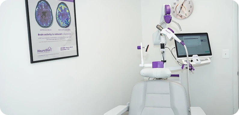 NeuroStar TMS device with purple and white components mounted above a treatment chair, with brain activity chart on wall
