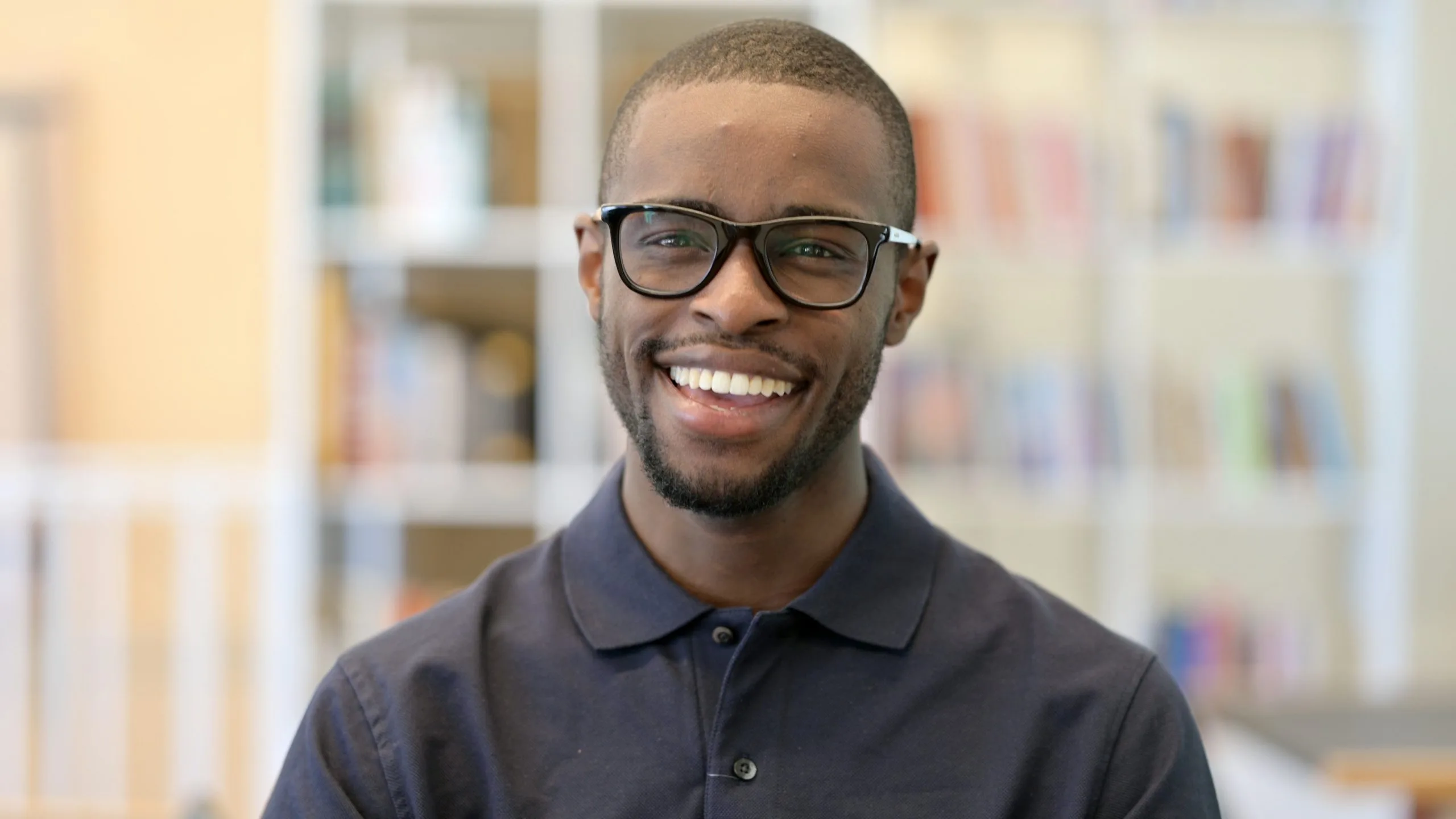 Smiling man wearing glasses in front of blurred bookshelf background