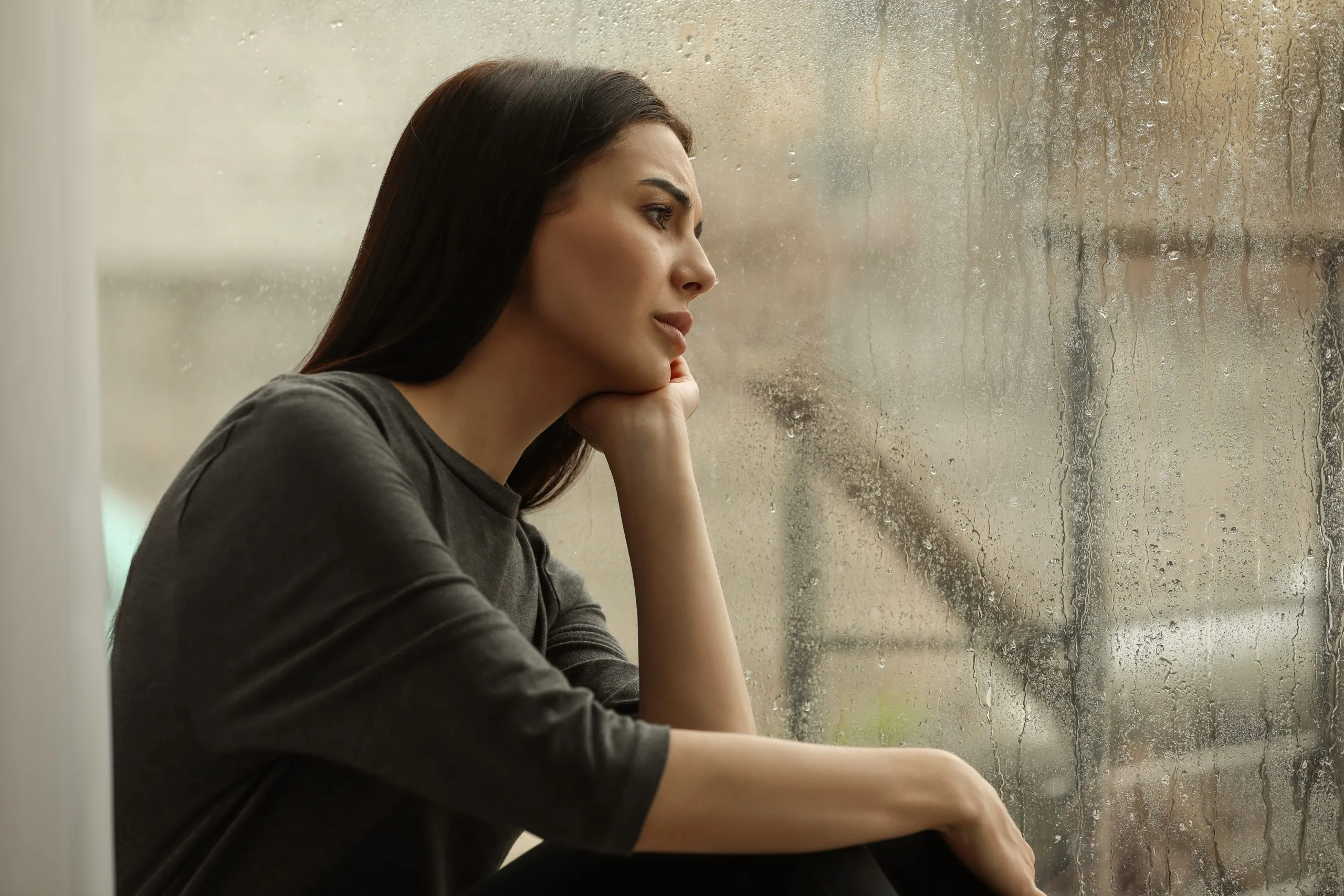 Woman in dark shirt leaning against a weathered concrete wall, looking to the side thoughtfully