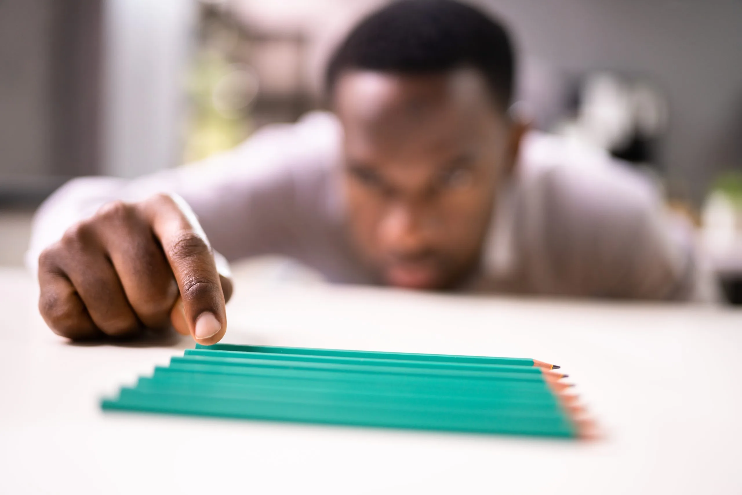 Person reaching toward a fanned arrangement of green pencils on a white surface