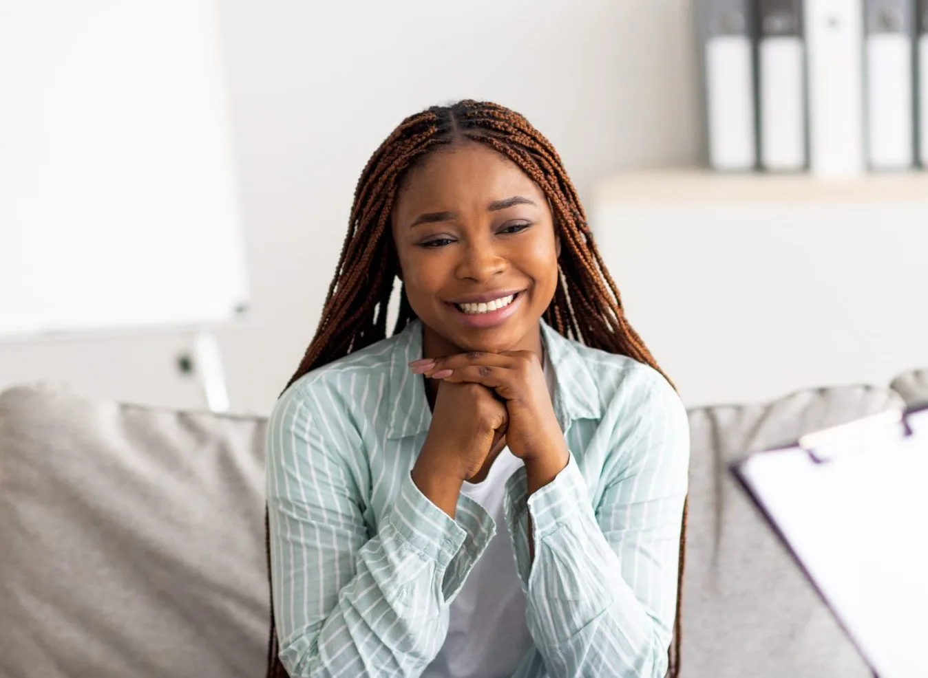 Woman smiling while sitting on couch with hands clasped near face