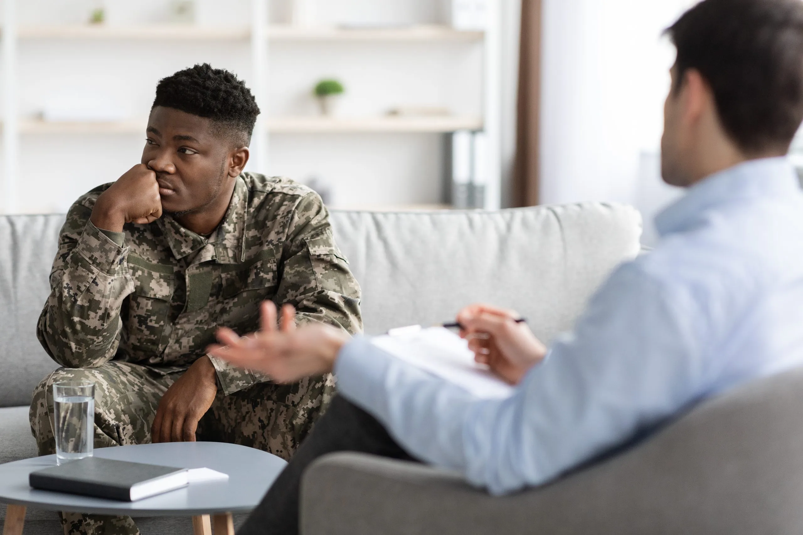 Service member in camouflage uniform speaking with counselor in blue shirt during session