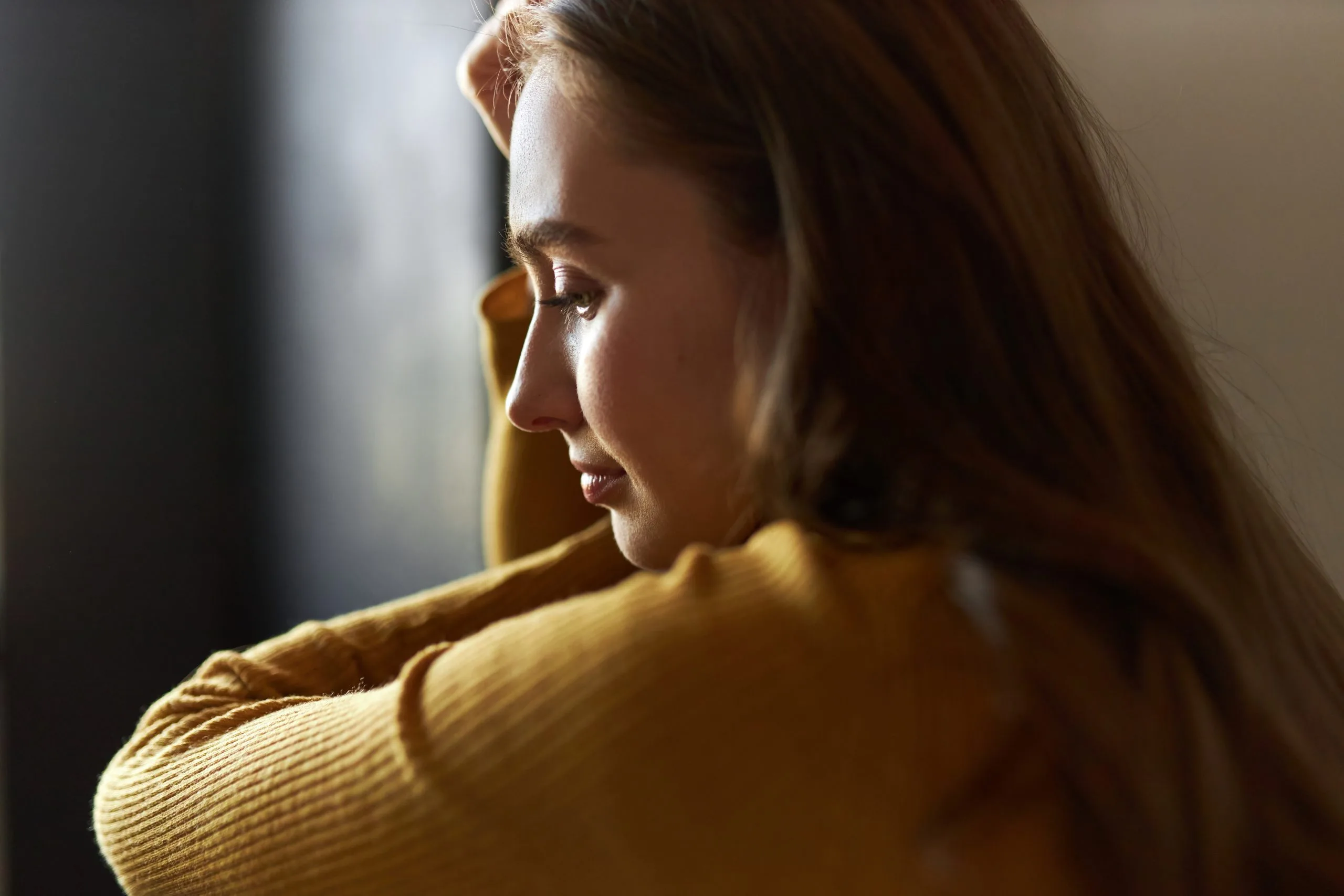 Woman in yellow shirt looking down pensively, hand near shoulder