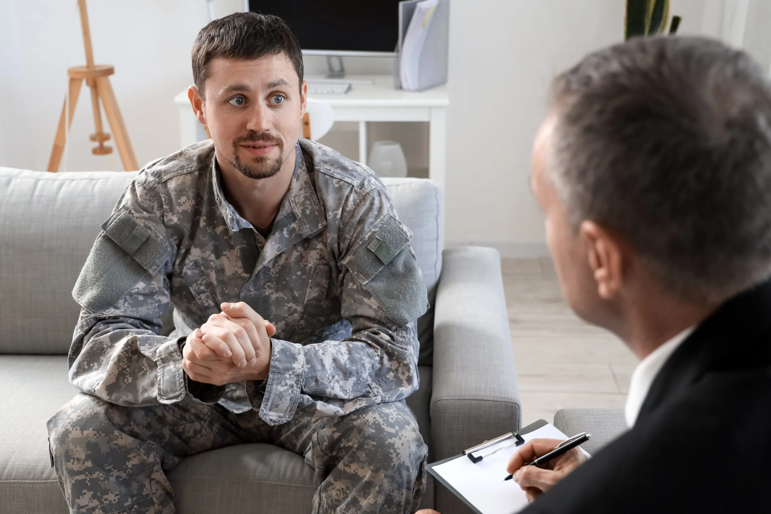 Male therapist taking notes while listening to male patient in military uniform during counseling session