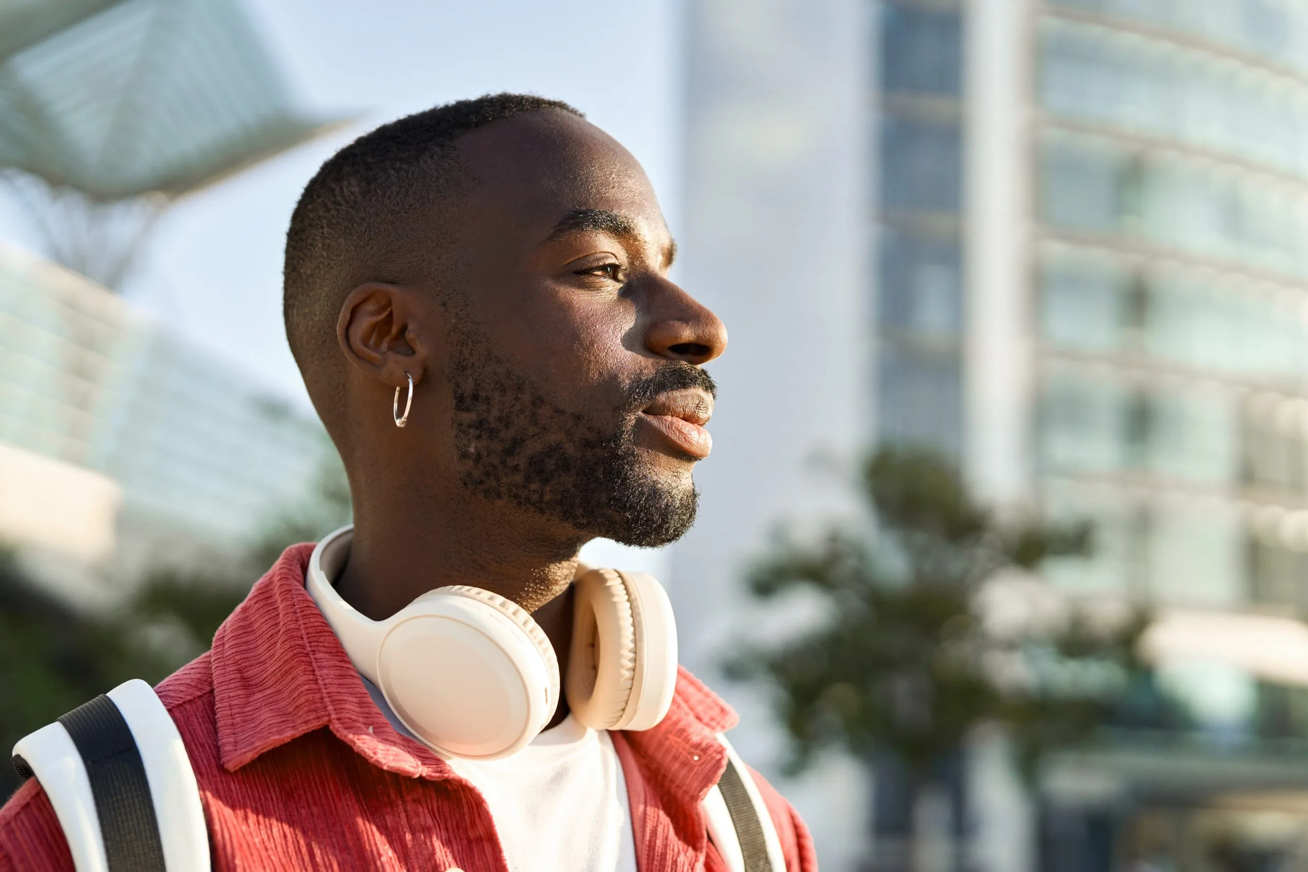 Man in red jacket wearing white headphones around neck in urban setting