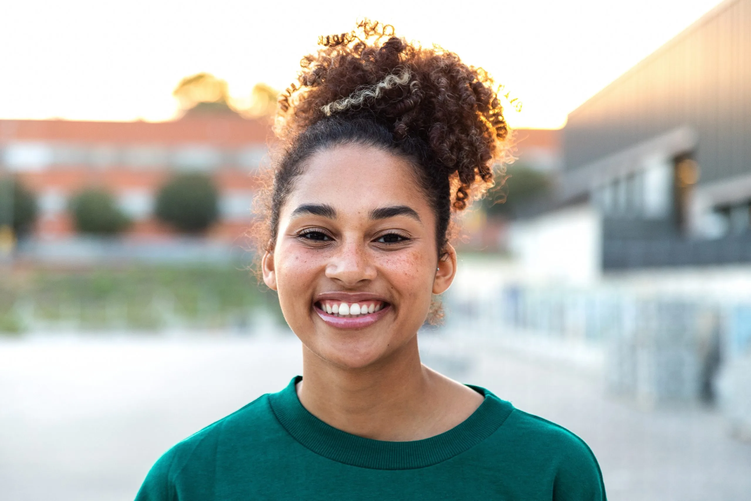 Smiling young woman in teal shirt at sunset with buildings in background