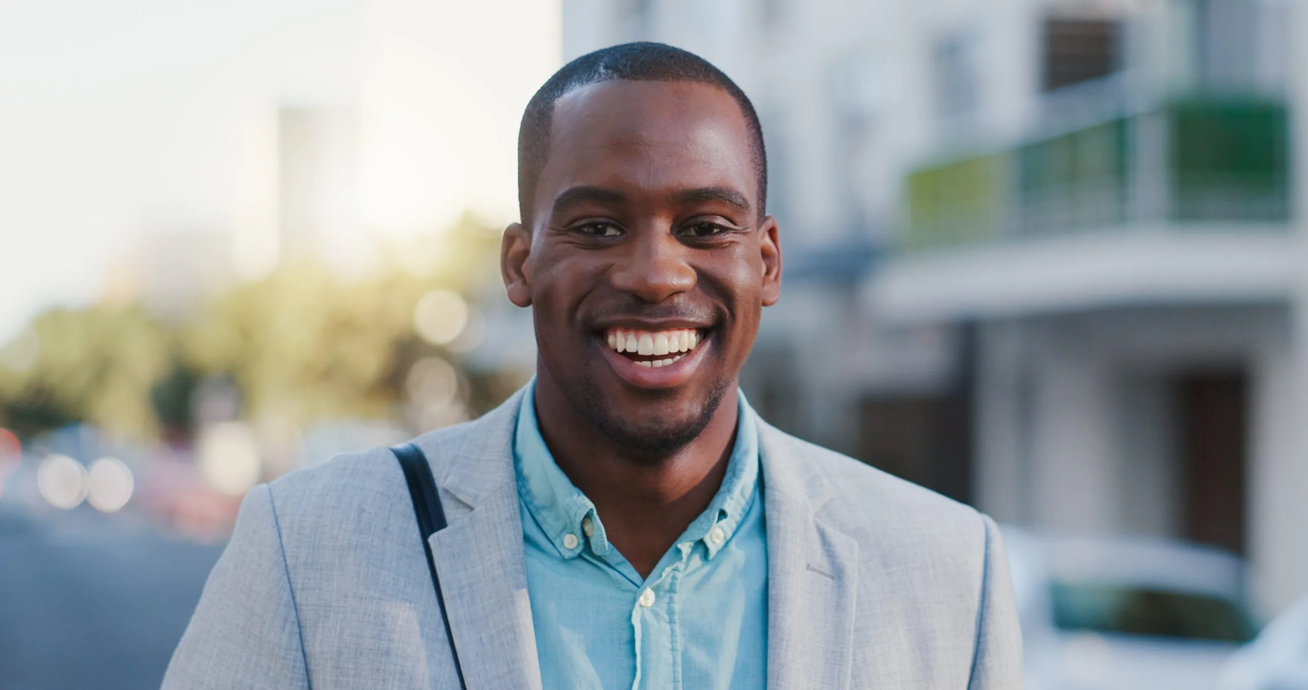 Smiling man in gray blazer and light blue shirt posing in front of modern building