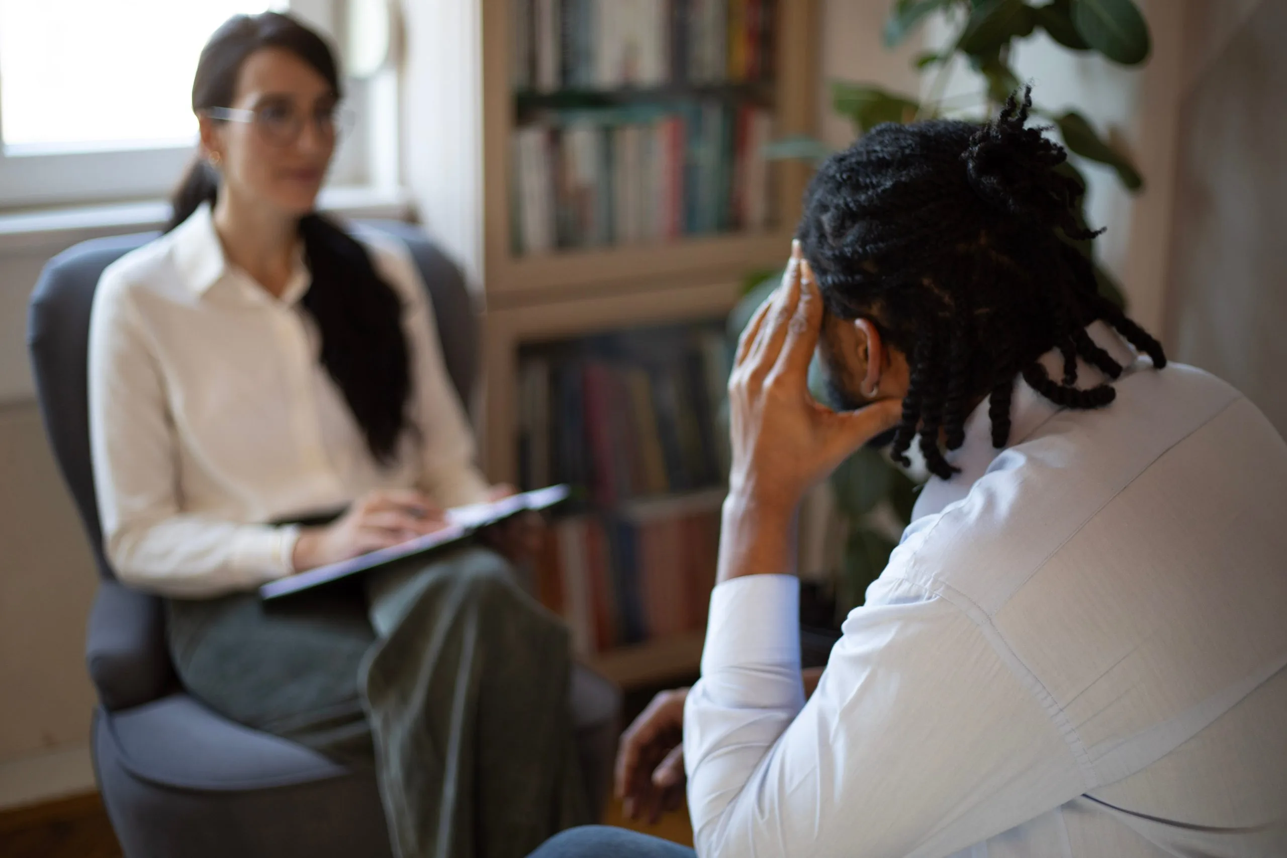 Therapist taking notes while patient sits across from her in office with bookshelves