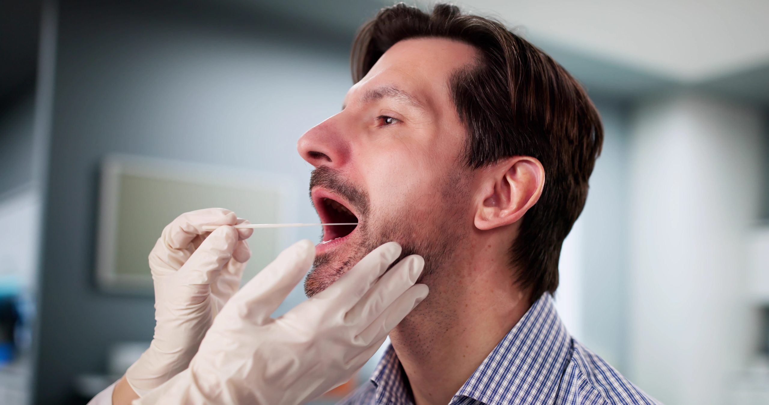 Dentist with gloved hands examining patient's open mouth in clinical setting