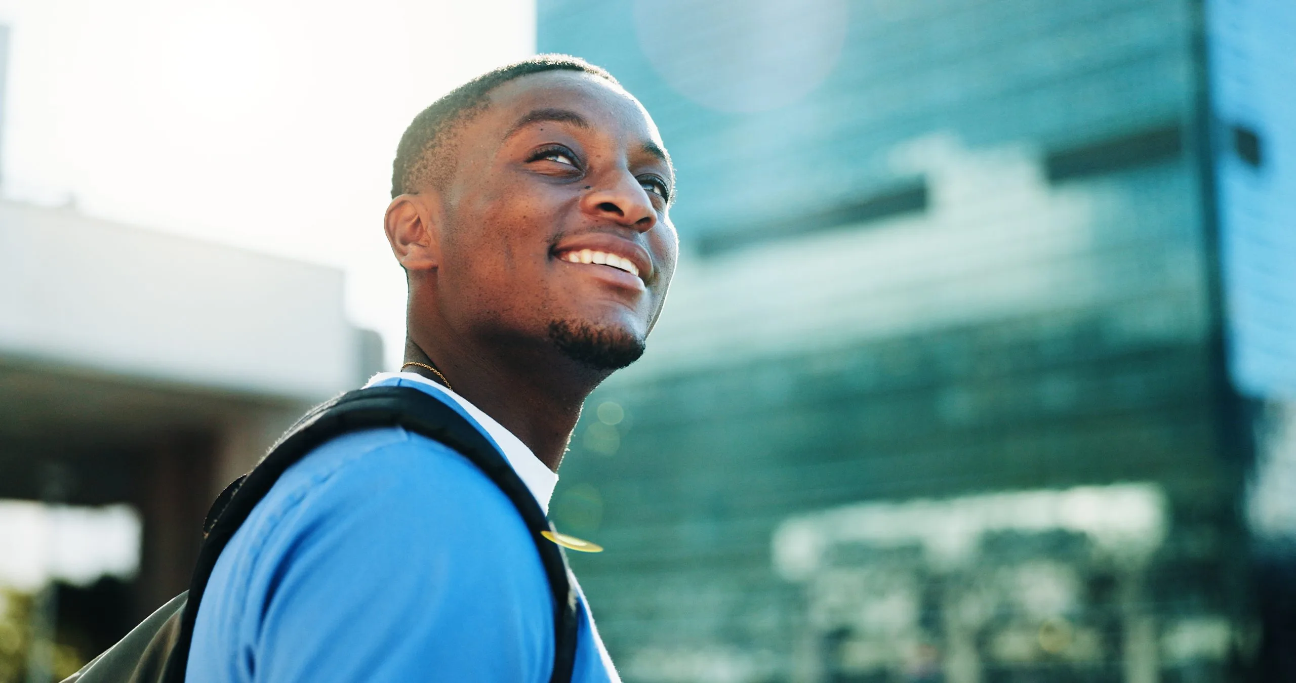 Smiling man in blue shirt outdoors with modern glass building visible in background