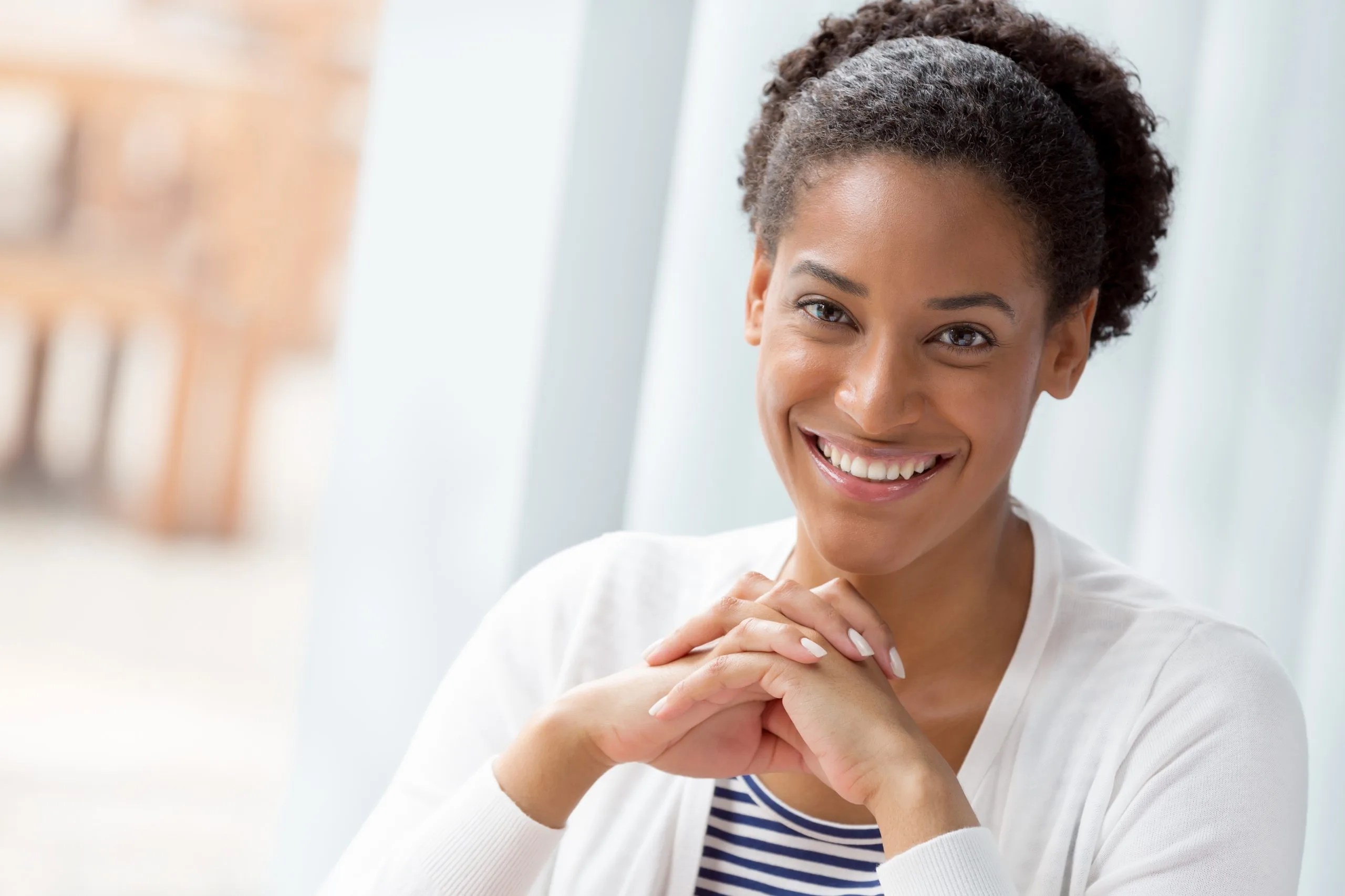 Woman smiling at camera with hands clasped near face in bright clinical setting