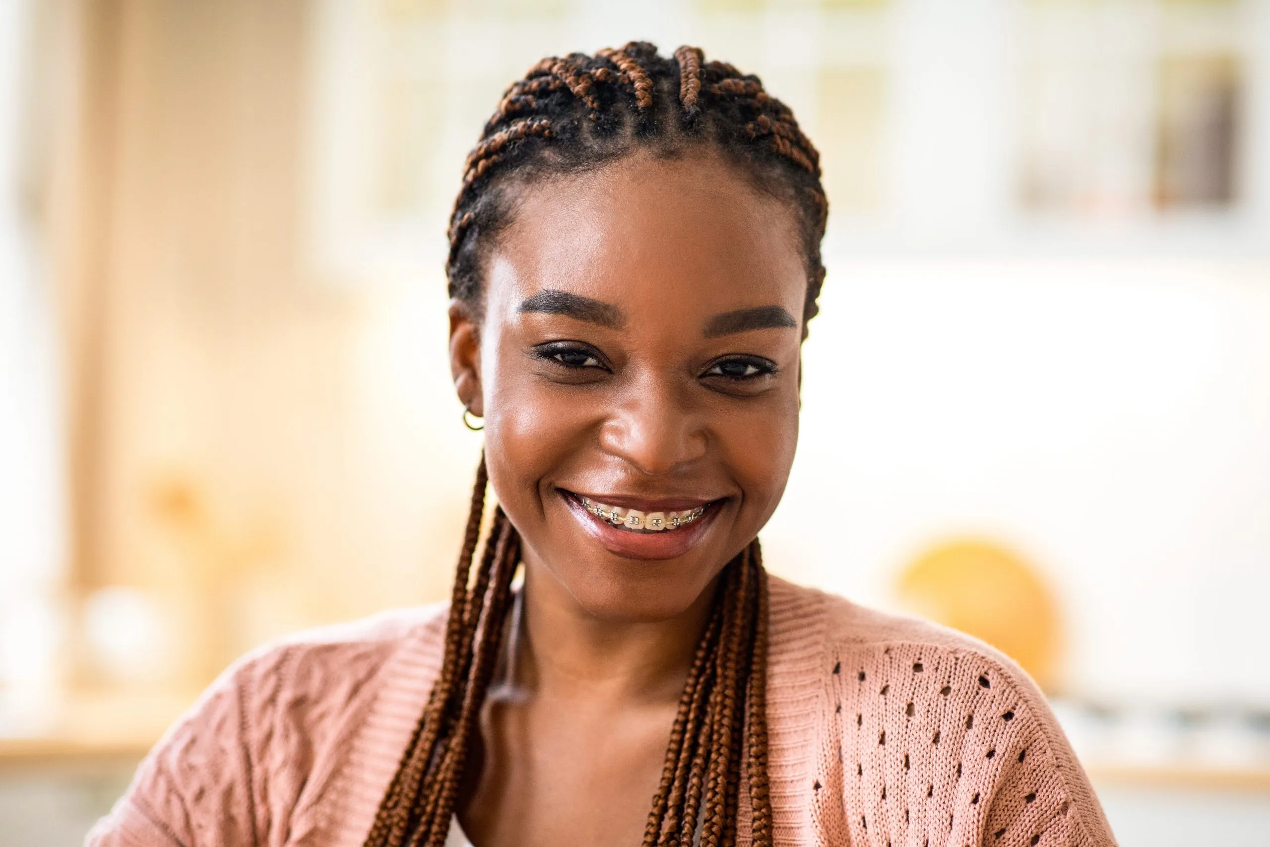 Young woman with braided hair wearing metal braces smiling brightly at camera