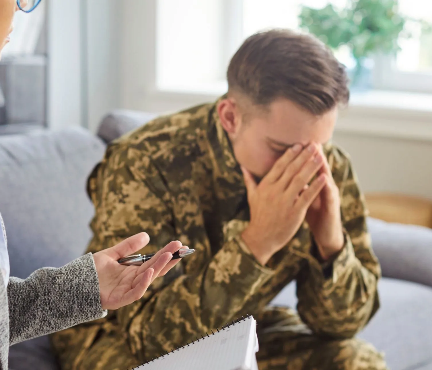 Therapist offering pen to distressed male patient in camouflage jacket during mental health consultation