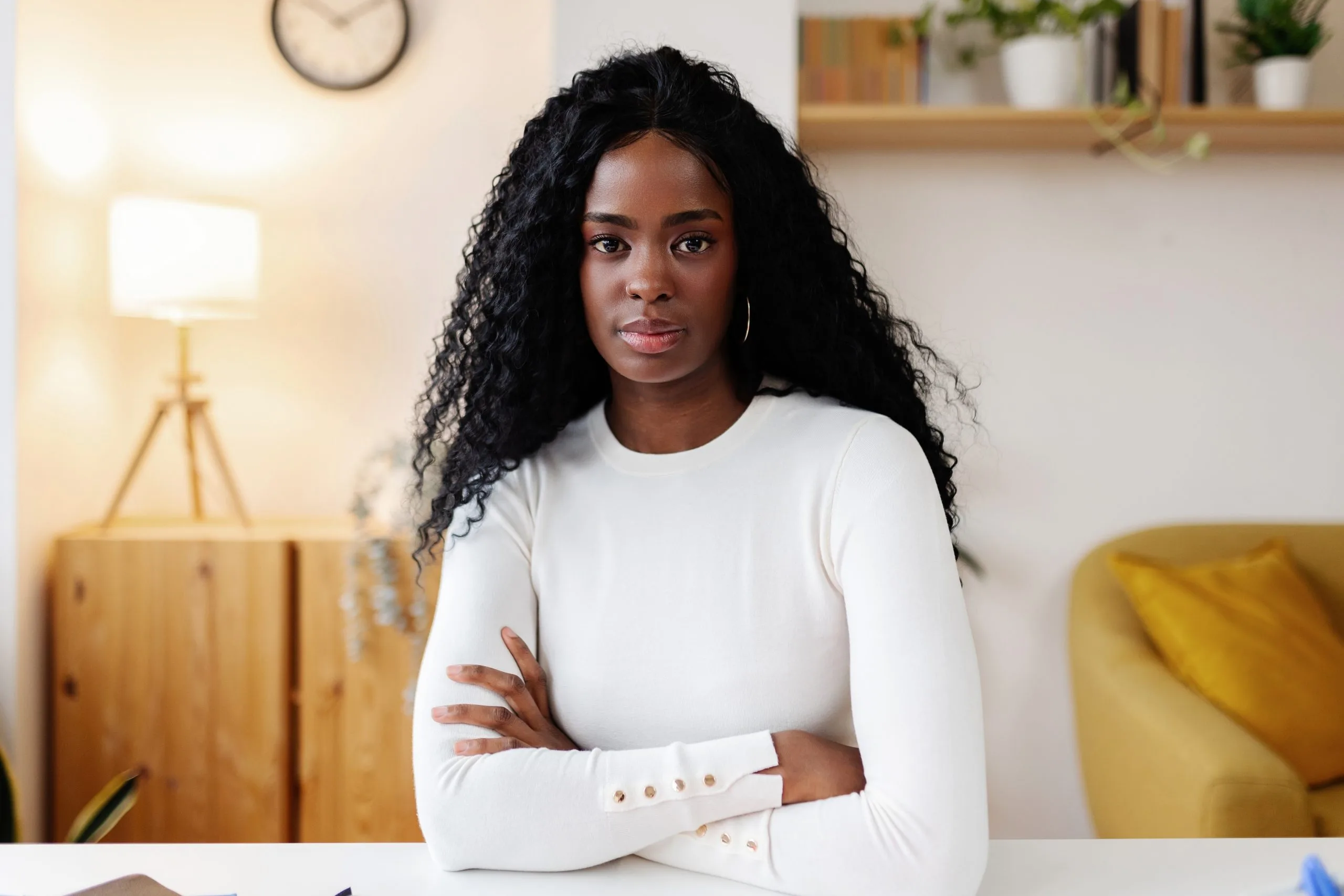Woman with arms crossed standing in modern office with warm lighting and wooden furniture