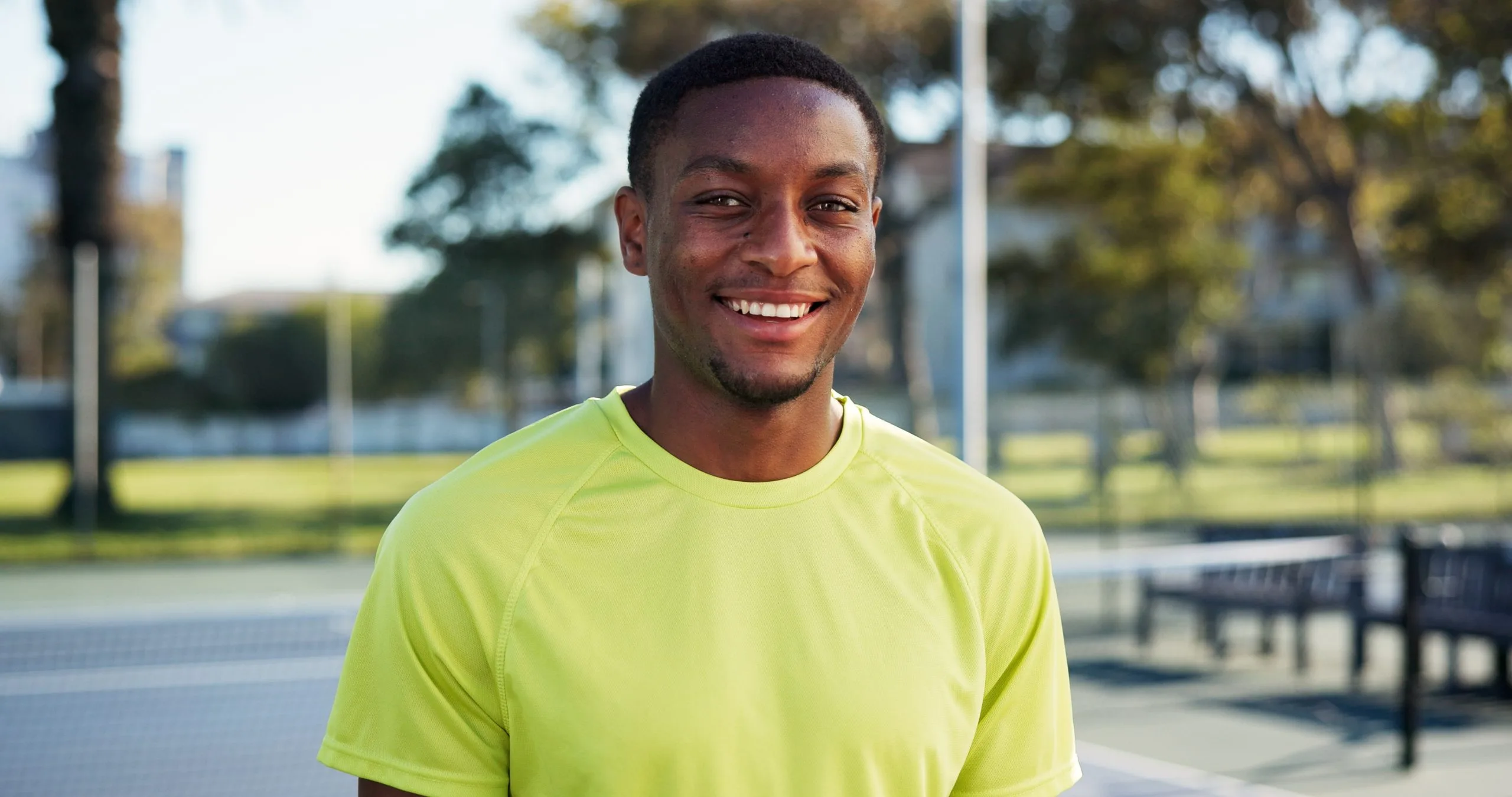 Smiling man in yellow shirt standing outdoors at a sports court