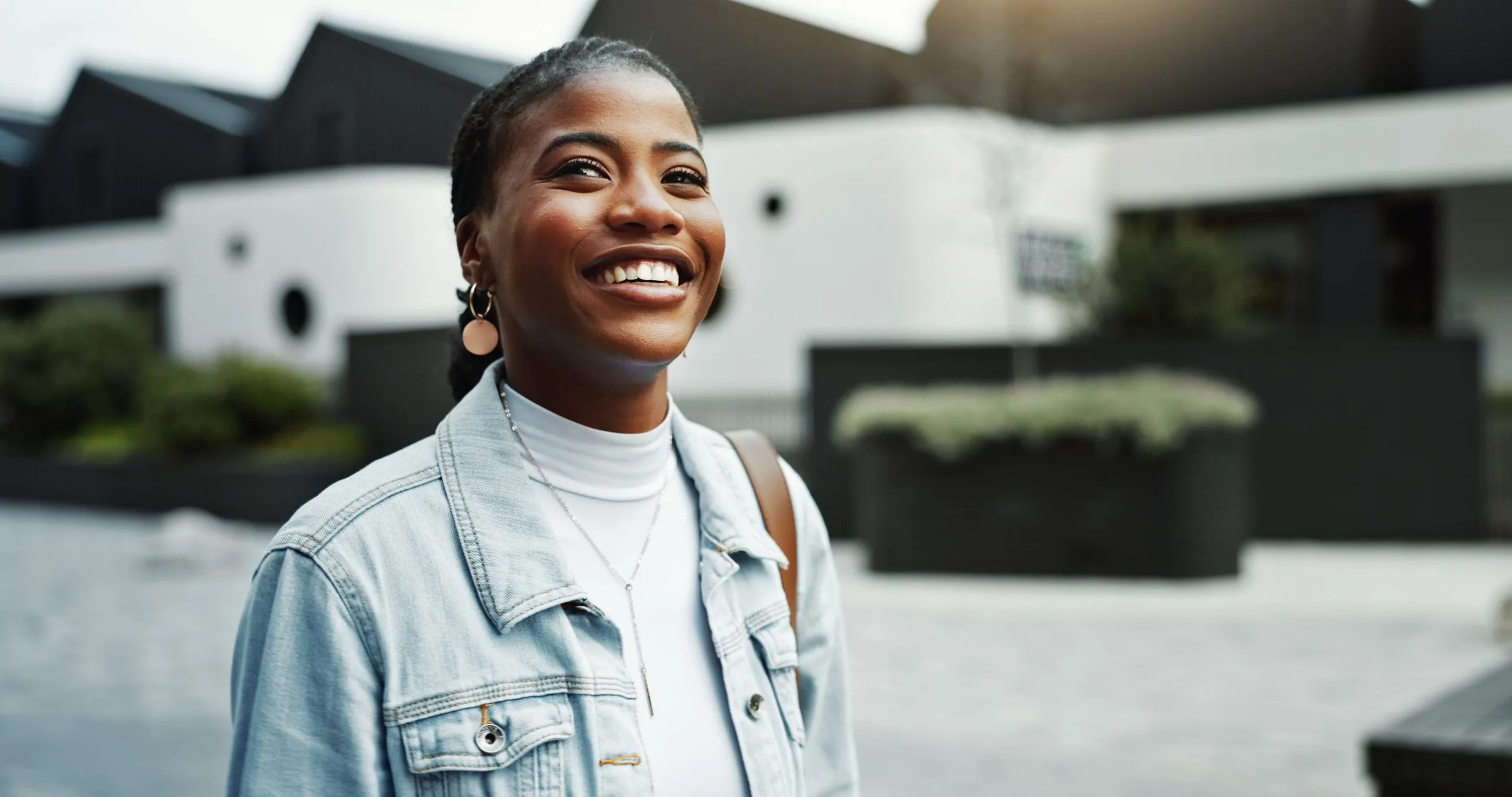 Smiling woman in denim shirt standing in front of modern white and black residential architecture