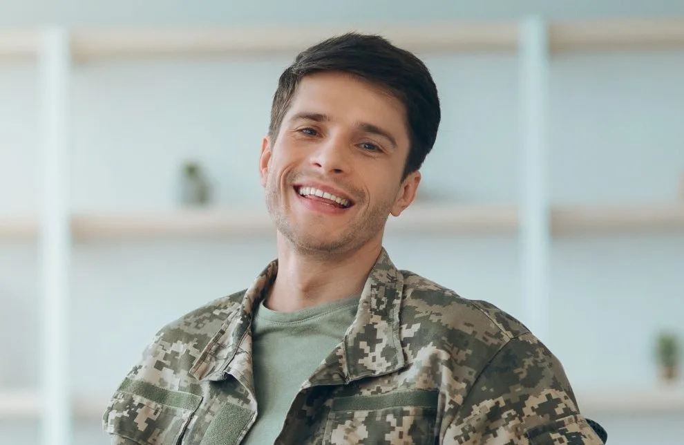 Military service member in camouflage jacket smiling in bright office setting