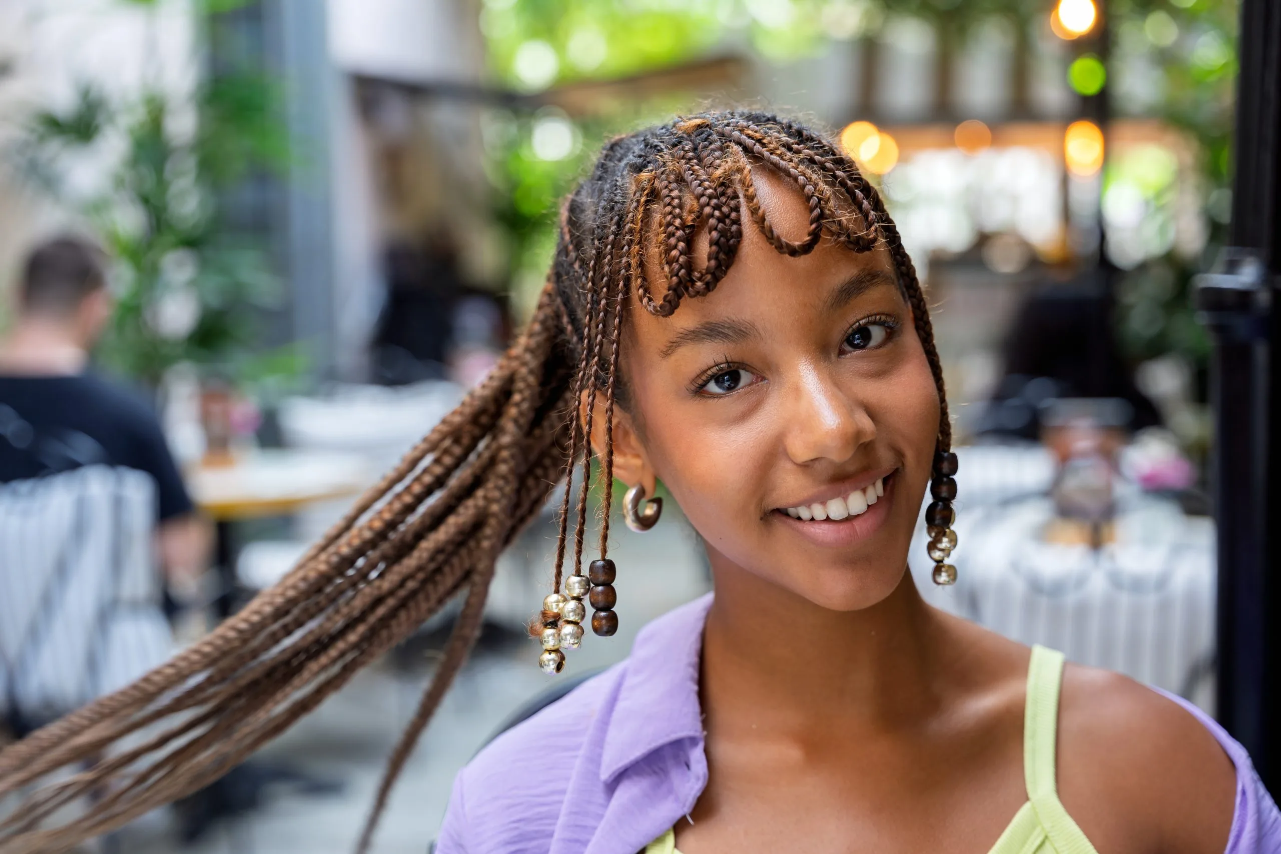 Young woman smiling at camera in outdoor venue wearing purple and green top with braided hairstyle