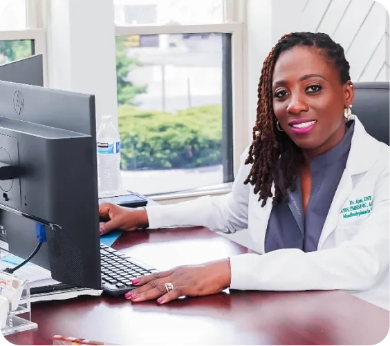 Healthcare provider in white coat at desk with computer in bright clinic office