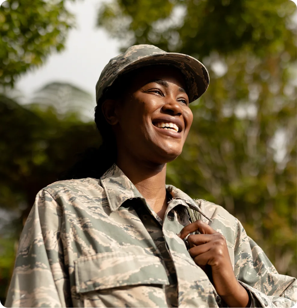 Service member in military uniform smiling outdoors under tree branches