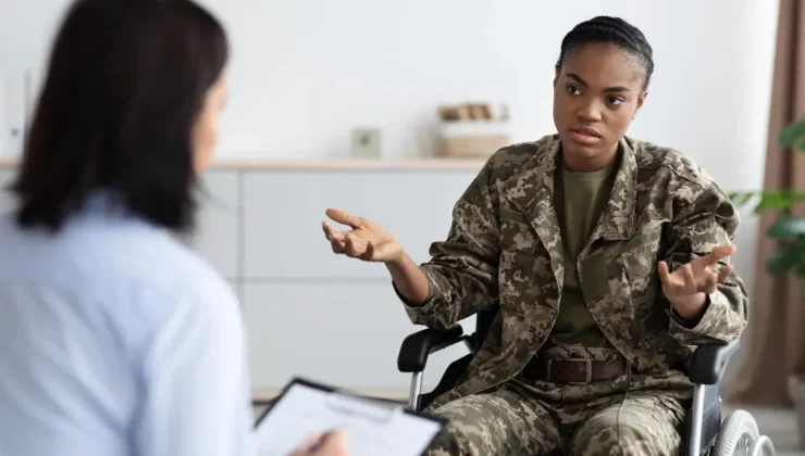 Service member in military camouflage uniform speaking with healthcare provider holding clipboard during consultation