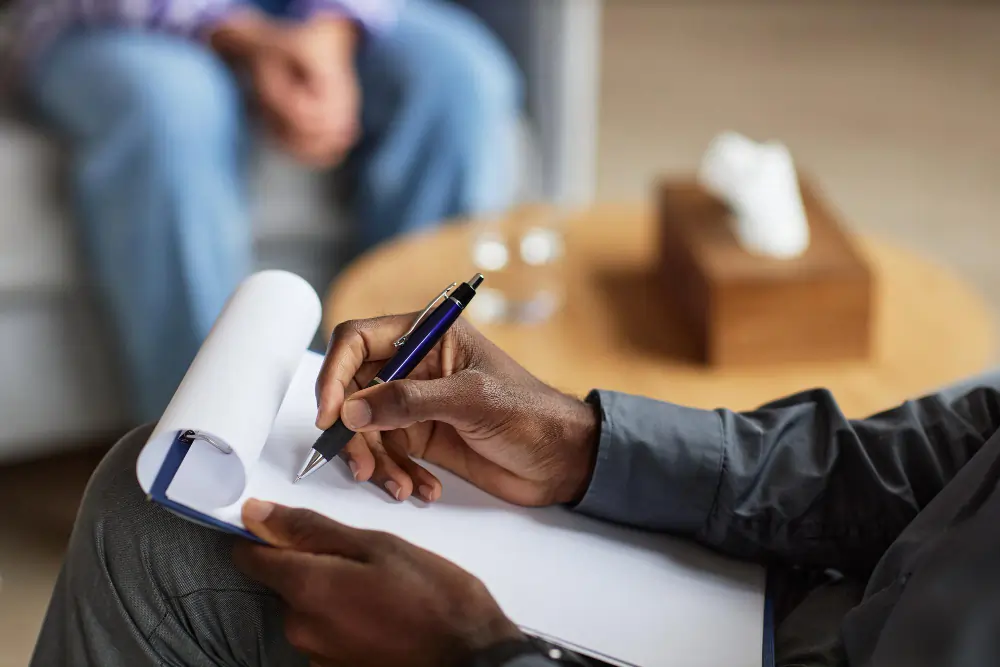 Therapist writing notes on clipboard during a mental health counseling session
