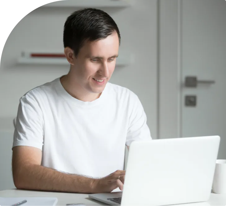 Man in white shirt smiling while using laptop at desk