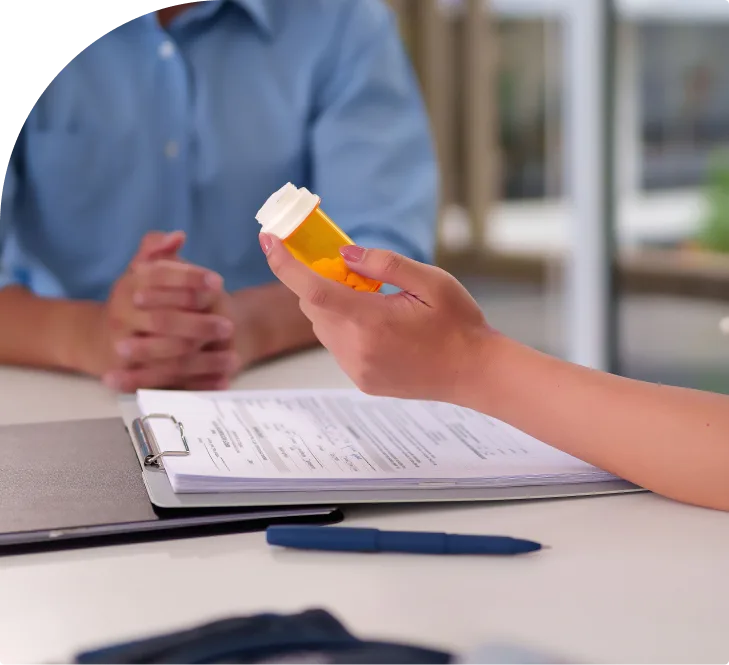Patient holding prescription medication bottle during consultation with healthcare provider and clipboard