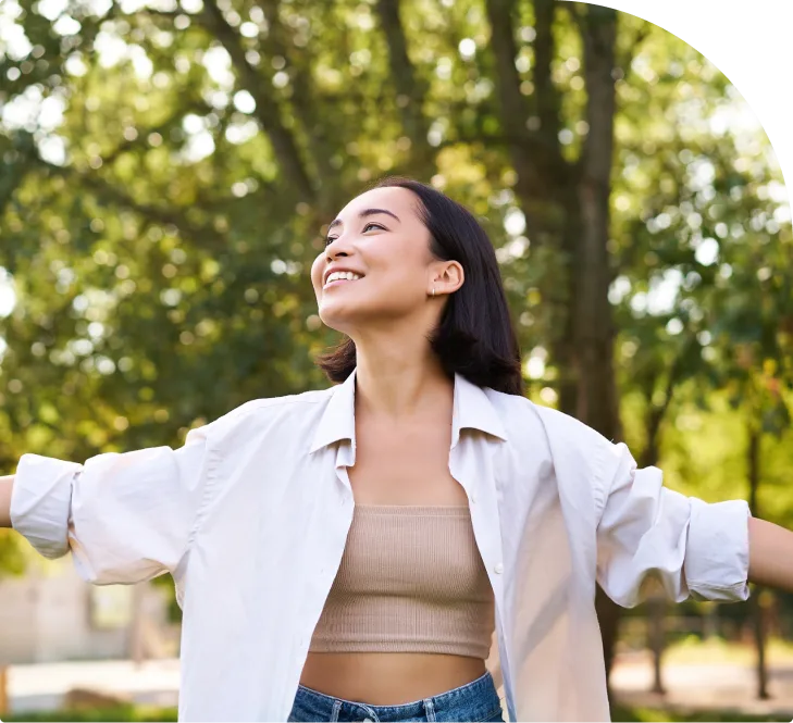 Woman in white shirt with arms outstretched smiling in park
