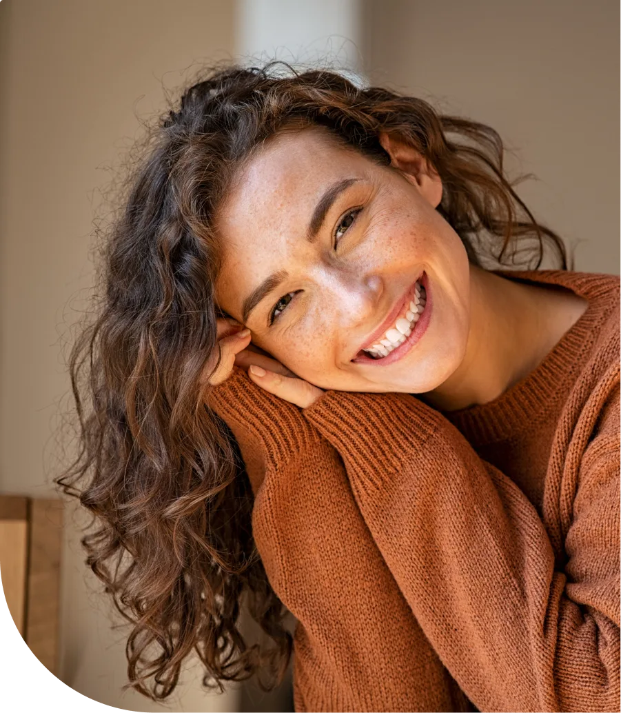 Woman with long dark curly hair smiling while hugging herself
