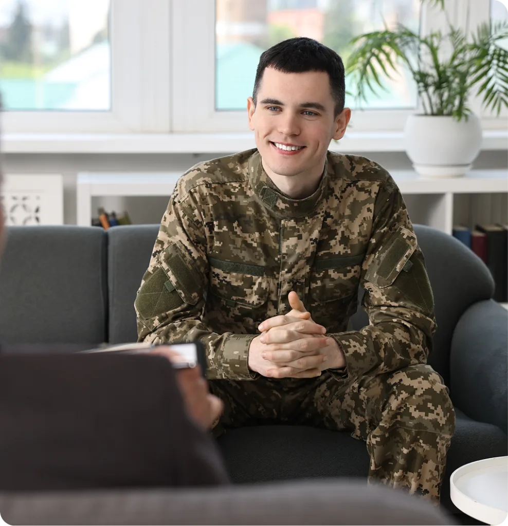 Smiling military service member in camouflage uniform sitting at laptop during telehealth session