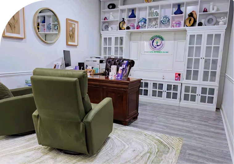 Mental health practice office with green armchair, wooden desk, wall-mounted shelving with decorative items, and framed artwork