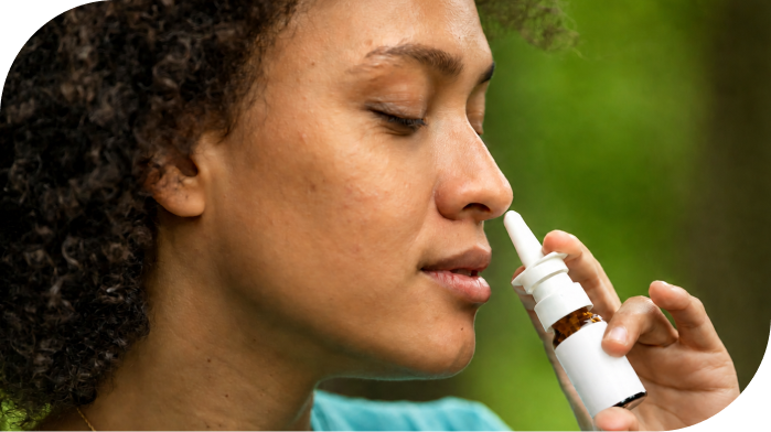 Person using a nasal spray applicator against a blurred green background