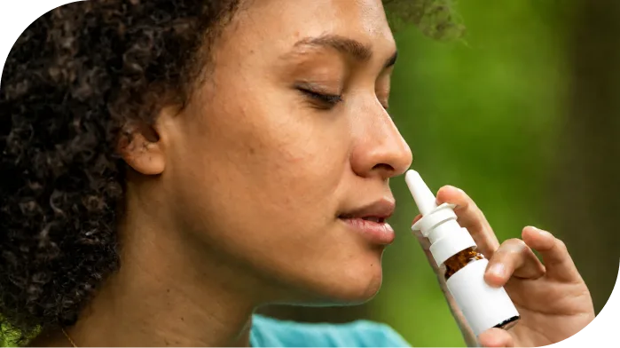 Person using a nasal spray applicator against a blurred green background